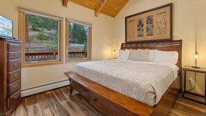 A bedroom with a wooden bed, two windows with a view of trees, a ceiling fan, and a nightstand with a lamp. - Quiet Fall River Suite • Fireplace • Close to RMNP (Estes Park)