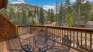 A wooden deck with a metal table and chairs, overlooking a forested hillside. - Quiet Fall River Suite • Fireplace • Close to RMNP (Estes Park)