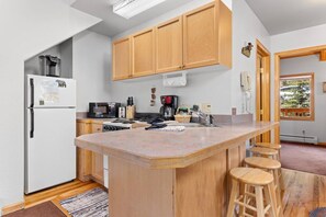 Una cocina con armarios de madera, una isla central con taburetes, un refrigerador, una estufa y un microondas.