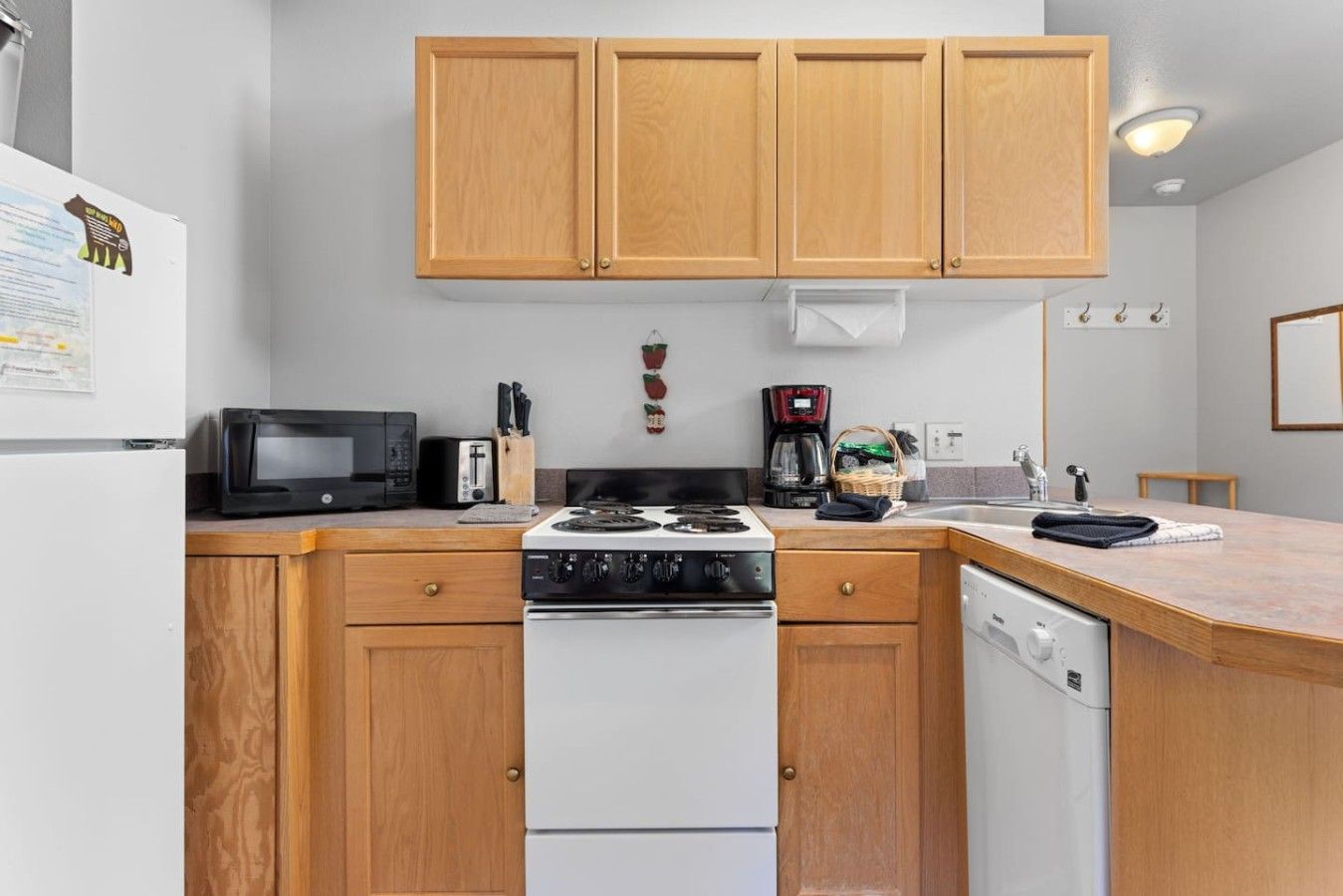 Cocina compacta con armarios de madera, microondas, tostadora, cafetera y lavavajillas.