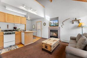 Une cuisine moderne avec des meubles en bois, une cuisinière et un petit îlot central. On y trouve également un espace salon avec un canapé et une cheminée.