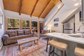 A cozy living room with a sofa, coffee table, and a dining area with a kitchen island. - Riverside Sanctuary • RMNP • River Views (Estes Park)