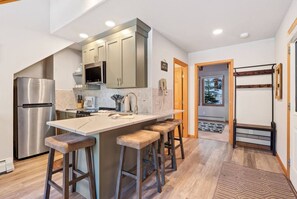 A modern kitchen with a stainless steel refrigerator, a large island with stools, and wooden cabinets. - Riverside Sanctuary • RMNP • River Views (Estes Park)