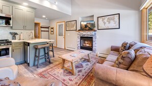 A spacious living area with a fireplace, a kitchen with a bar, and a cozy seating area. - Riverside Sanctuary • RMNP • River Views (Estes Park)