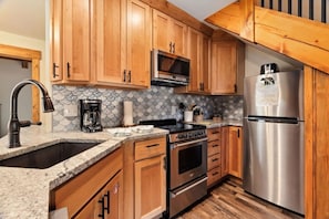 A kitchen with wooden cabinets, a stainless steel refrigerator, a microwave, a stove, and a granite countertop. - Whispering River Escape • Private Hot Tub • RMNP (Estes Park)