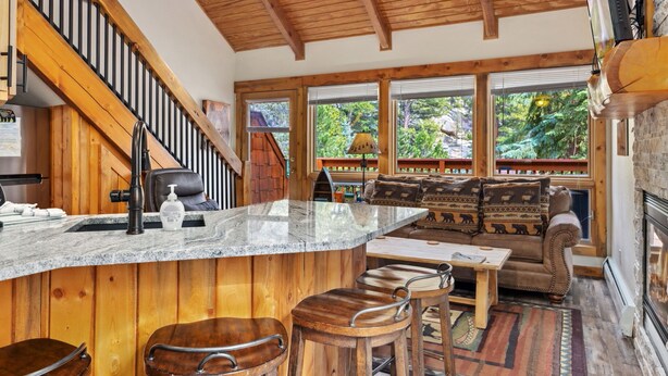 A cozy kitchen with a wooden island, bar stools, and a large window overlooking greenery. - Whispering River Escape • Private Hot Tub • RMNP (Estes Park)