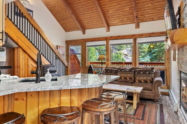 A wooden interior with a kitchen area, bar stools, a sofa, and a fireplace. - Whispering River Escape • Private Hot Tub • RMNP (Estes Park)