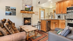 A cozy living room with a fireplace, a dining area, and a kitchen with wooden cabinets and modern appliances. - Whispering River Escape • Private Hot Tub • RMNP (Estes Park)