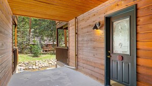 Une cabane en bois avec une porte sombre, un petit porche et une vue sur une zone boisée.