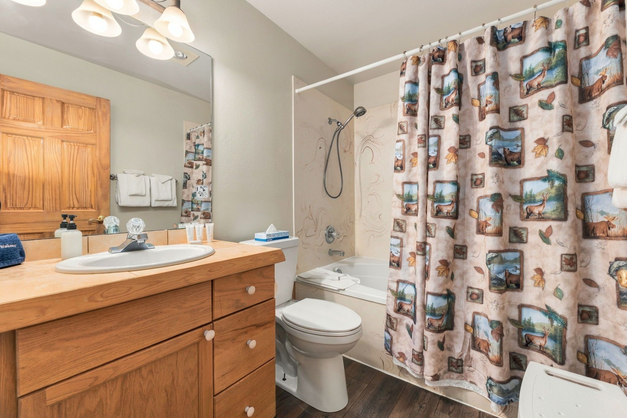 A bathroom with a wooden vanity, a toilet, a shower with a curtain, and a mirror.