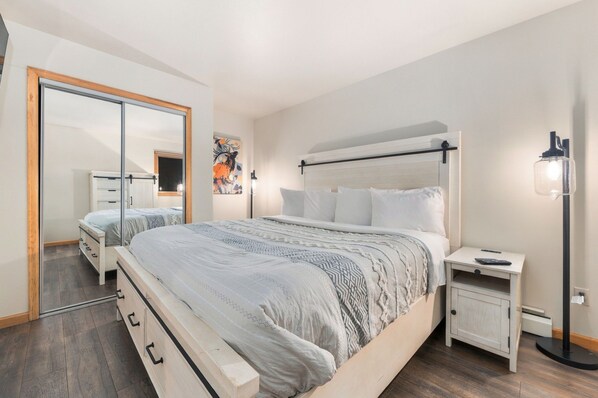 A modern bedroom with a large bed, bedside tables, a wardrobe, and a mirror.