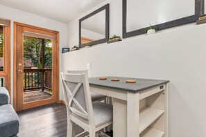 A room with a wooden door, a white chair, a table with a grey top, and a shelf with plants. - Fall River Hideaway • River Views • Close to RMNP (Estes Park)