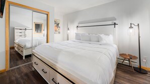 Une chambre à coucher moderne avec un grand lit, un miroir, une table de chevet et une lampe sur pied.
