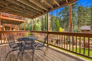 A wooden deck with a table and chairs, overlooking a forested area.
