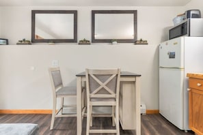 A small kitchenette with a refrigerator, microwave, and a coffee maker. There is a dining table with two chairs and two wall-mounted mirrors above it. - Fall River Hideaway • River Views • Close to RMNP (Estes Park)
