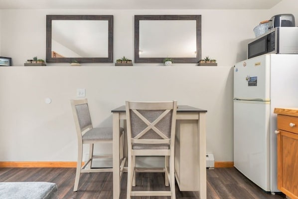 A small kitchenette with a refrigerator, microwave, and a coffee maker. There is a dining table with two chairs and two wall-mounted mirrors above it.