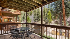 Une terrasse en bois avec une table et des chaises, donnant sur une zone boisée traversée par un ruisseau.