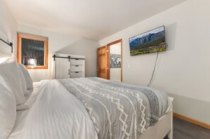 Ein Schlafzimmer mit einem Bett, einem Schminktisch, einem Fenster mit Lampe und einem Fernseher an der Wand.