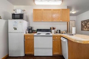 A compact kitchen with a refrigerator, microwave, stove, wooden cabinets, and a countertop.