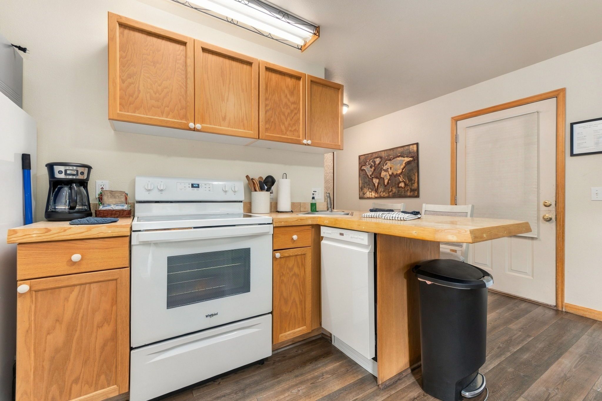 Una cocina compacta con armarios de madera, una estufa blanca, un lavavajillas y un cubo de basura.