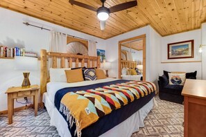 Un dormitorio con techo de madera, una cama con manta de colores, una mesita de noche, un aparador y un espejo.