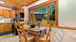 A wooden kitchen with a dining area, large windows, and a view of a cabin. - Fall River Retreat • Private Hot Tub • Close to RMNP (Estes Park)