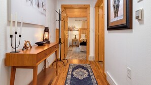 A hallway with wooden flooring, a blue patterned rug, a wooden console table with a clock, candles, and a lantern. - Fall River Retreat • Private Hot Tub • Close to RMNP (Estes Park)