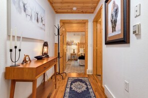 A hallway with a wooden floor, a rug, a coat rack, a desk with a candelabra, and a framed picture on the wall. - Fall River Retreat • Private Hot Tub • Near RMNP (Estes Park)