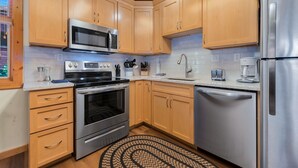 A modern kitchen with wooden cabinets, stainless steel appliances, and a patterned rug. - Updated Riverfront Retreat • A/C • Private Hot Tub (Estes Park)