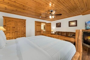 A bedroom with a large bed, wooden ceiling, a fireplace, and a ceiling fan. - Updated Riverfront Retreat • A/C • Private Hot Tub (Estes Park)