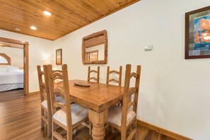 A wooden dining table with six chairs, a mirror on the wall, and a bed in the adjacent room. - Updated Riverfront Retreat • A/C • Private Hot Tub (Estes Park)