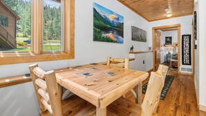 A wooden dining table with chairs, a view of a forest through a window, and a 'WELCOME' sign. - River Retreat • River Views • Near RMNP (Estes Park)