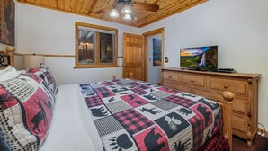 A bedroom with a bed, a wooden dresser, a television, a ceiling fan, and a window.