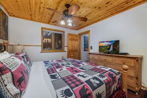 A bedroom with a bed, a wooden dresser, a television, a ceiling fan, and a window.