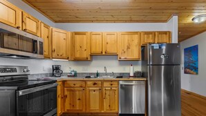 A modern kitchen with wooden cabinets, stainless steel appliances, and a wooden floor.