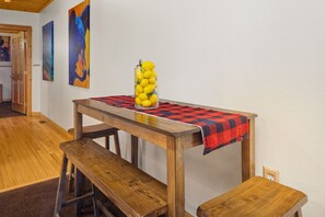 Une table de salle à manger en bois, recouverte d’une nappe à carreaux rouges et noirs, avec des bancs et un vase en verre contenant des fleurs jaunes.