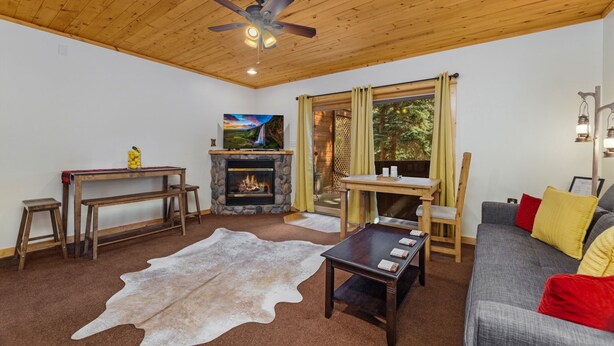 A cozy living room with a fireplace, a television, a ceiling fan, and a sofa.