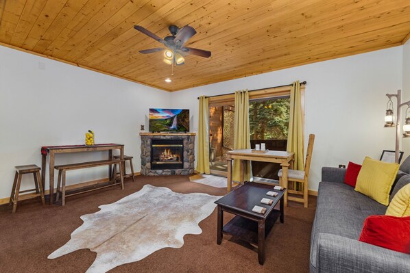 A cozy living room with a fireplace, a television, a ceiling fan, and a sofa.