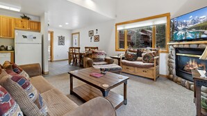 Uma sala de estar ampla com lareira, uma janela grande com vista para as montanhas e um ambiente aconchegante para sentar.