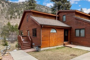 A two-story wooden cabin with a covered porch, a visible staircase, and a view of a mountainous landscape. - Fall River Retreat • Private Hot Tub (Estes Park)