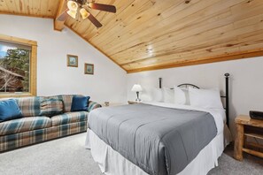 A bedroom with a bed, a wooden ceiling, a window, and a plaid sofa. - Fall River Retreat • Private Hot Tub (Estes Park)