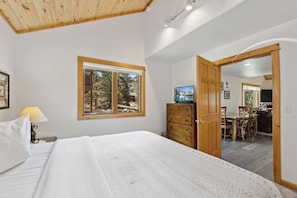 A bedroom with a bed, a dresser, a television, and a window with a view of trees. - Fall River Retreat • Private Hot Tub (Estes Park)