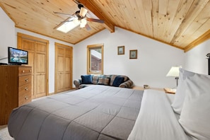 Een slaapkamer met een bed, een televisie, houten kasten, een plafondventilator en een raam.