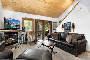 A cozy living room with a fireplace, leather sofa, and a television displaying a mountain scene.