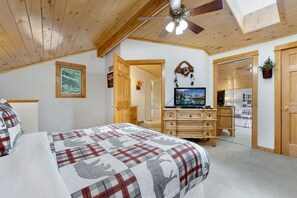 Une chambre à coucher comprenant un lit, une commode, un téléviseur et un ventilateur de plafond.