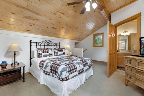A bedroom with a bed, bedside lamps, a dresser, a ceiling fan, and a window.