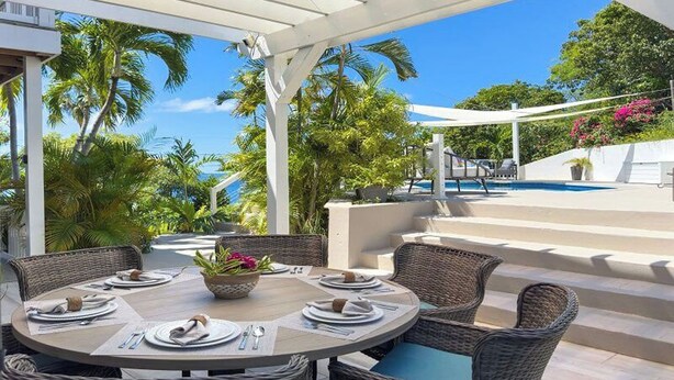 Un espace extérieur abrité, aménagé pour les repas, avec des meubles en osier, une piscine et une végétation tropicale.