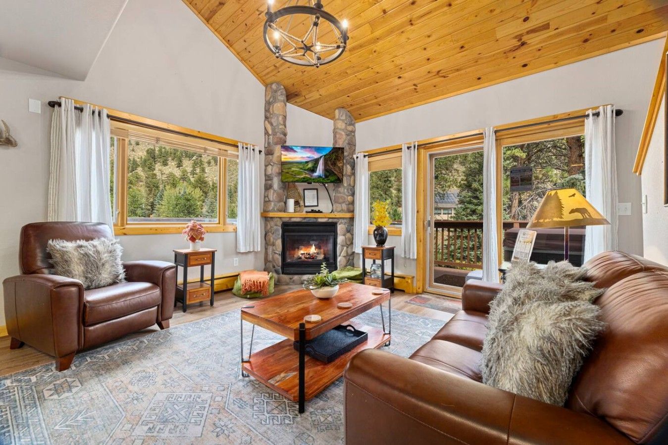 A spacious living room with leather sofas, a fireplace, and large windows offering a view of the outdoors.