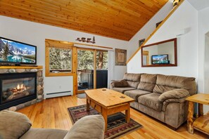 A cozy living room with a fireplace, a sofa, a coffee table, and a television. - Riverfront Hideaway • Private Hot Tub • Near RMNP (Estes Park)