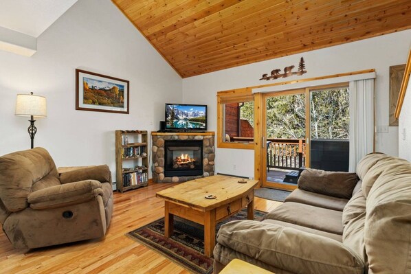 A cozy living room with a fireplace, a television, and a sofa. - Riverfront Hideaway • Private Hot Tub • Near RMNP (Estes Park)